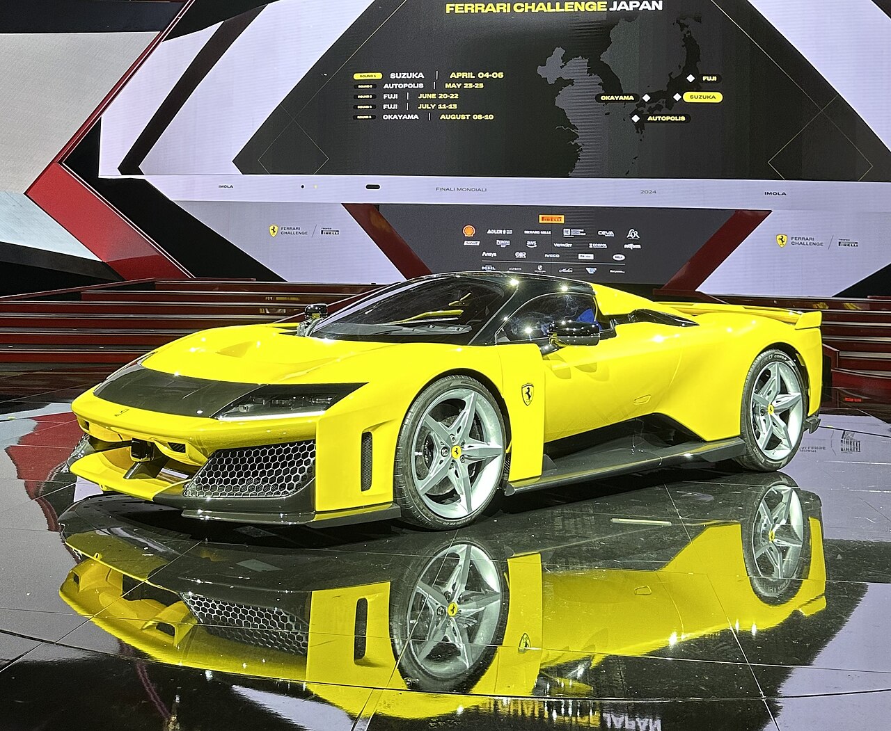 A yellow Ferrari supercar on a reflective stage in front of event screens reading Finali Mondiali and Imola