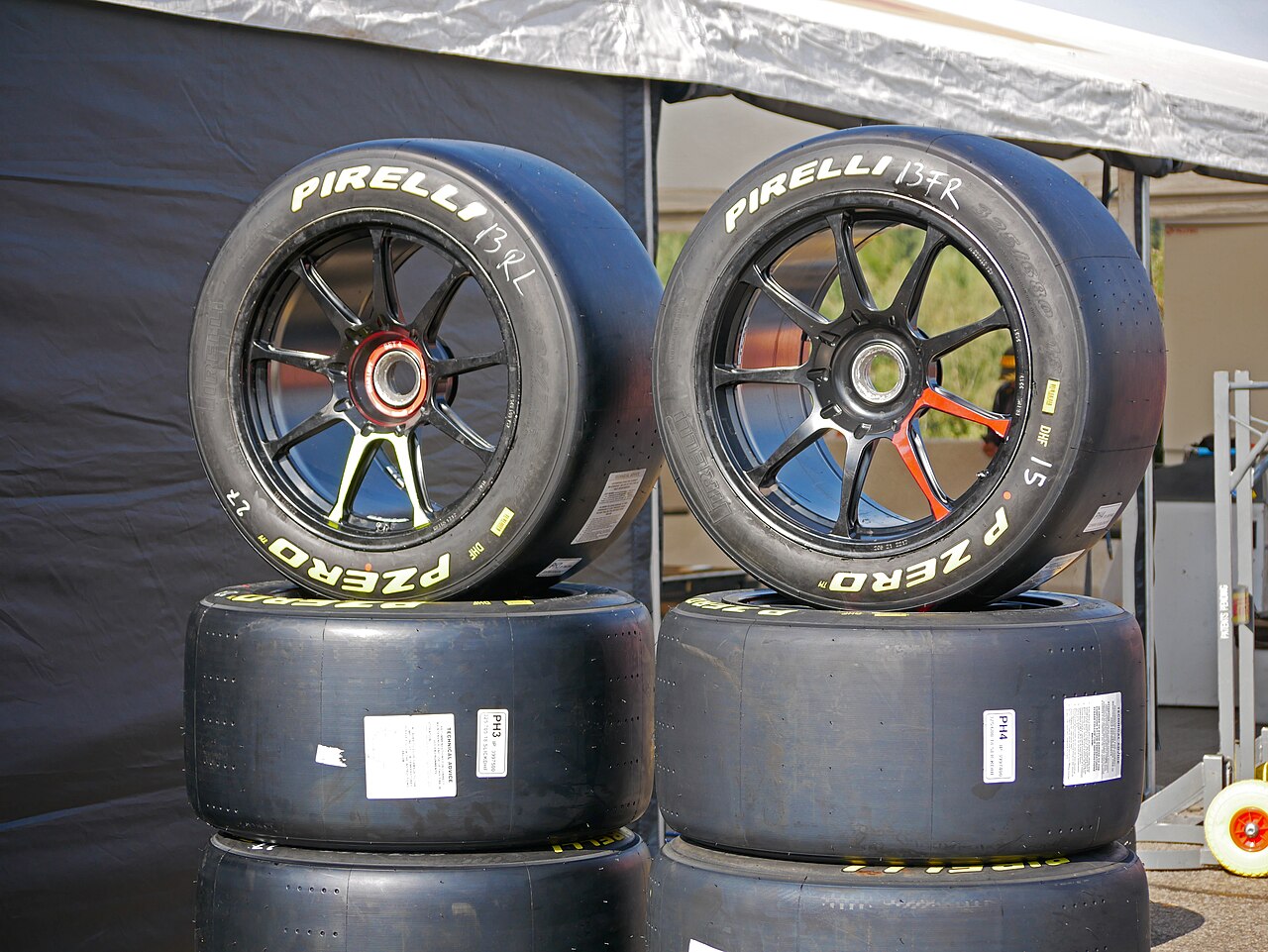 Stacks of racing tires and black wheels under a tent at a race track