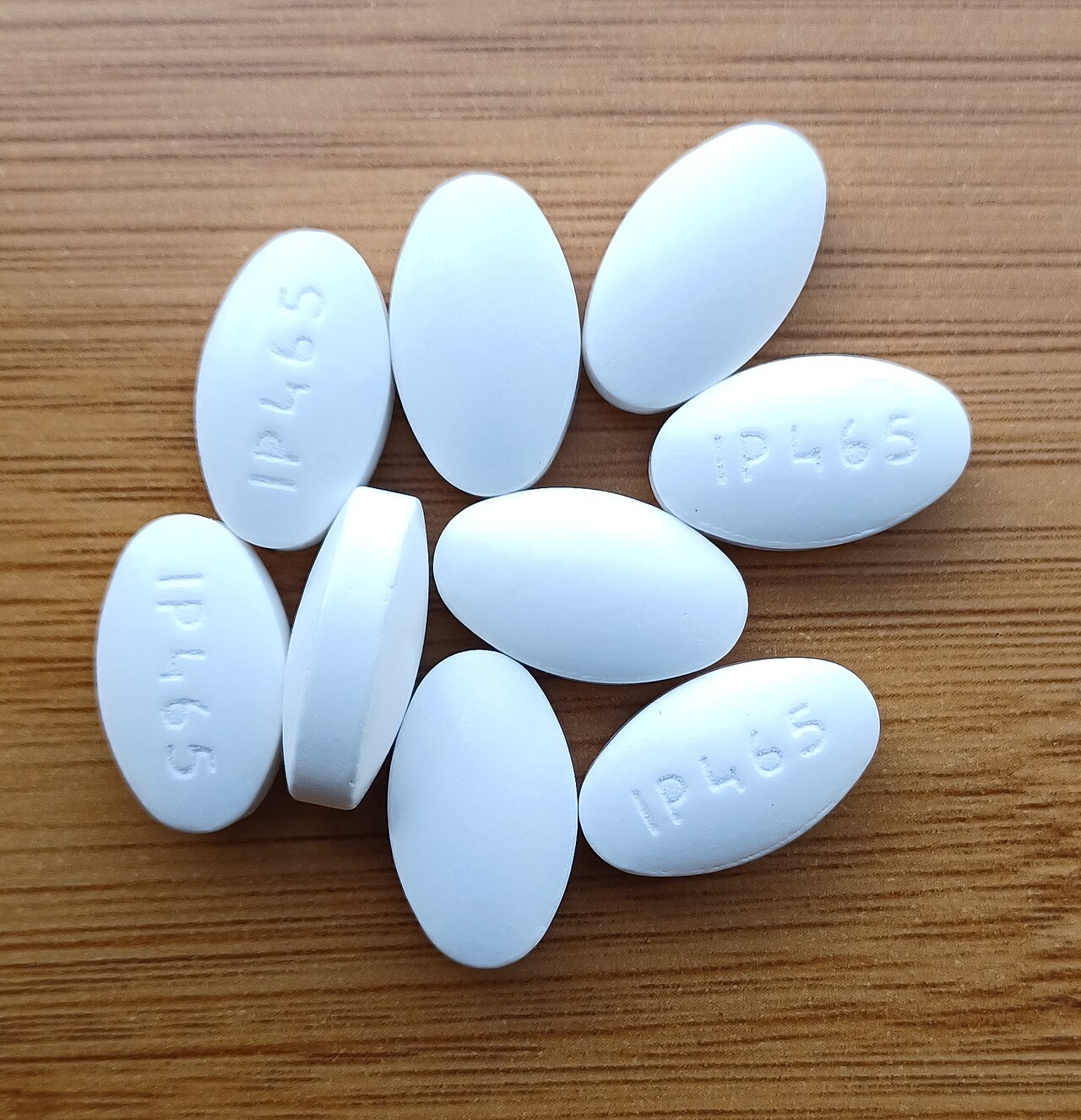 White oval pharmaceutical tablets arranged on a wooden surface